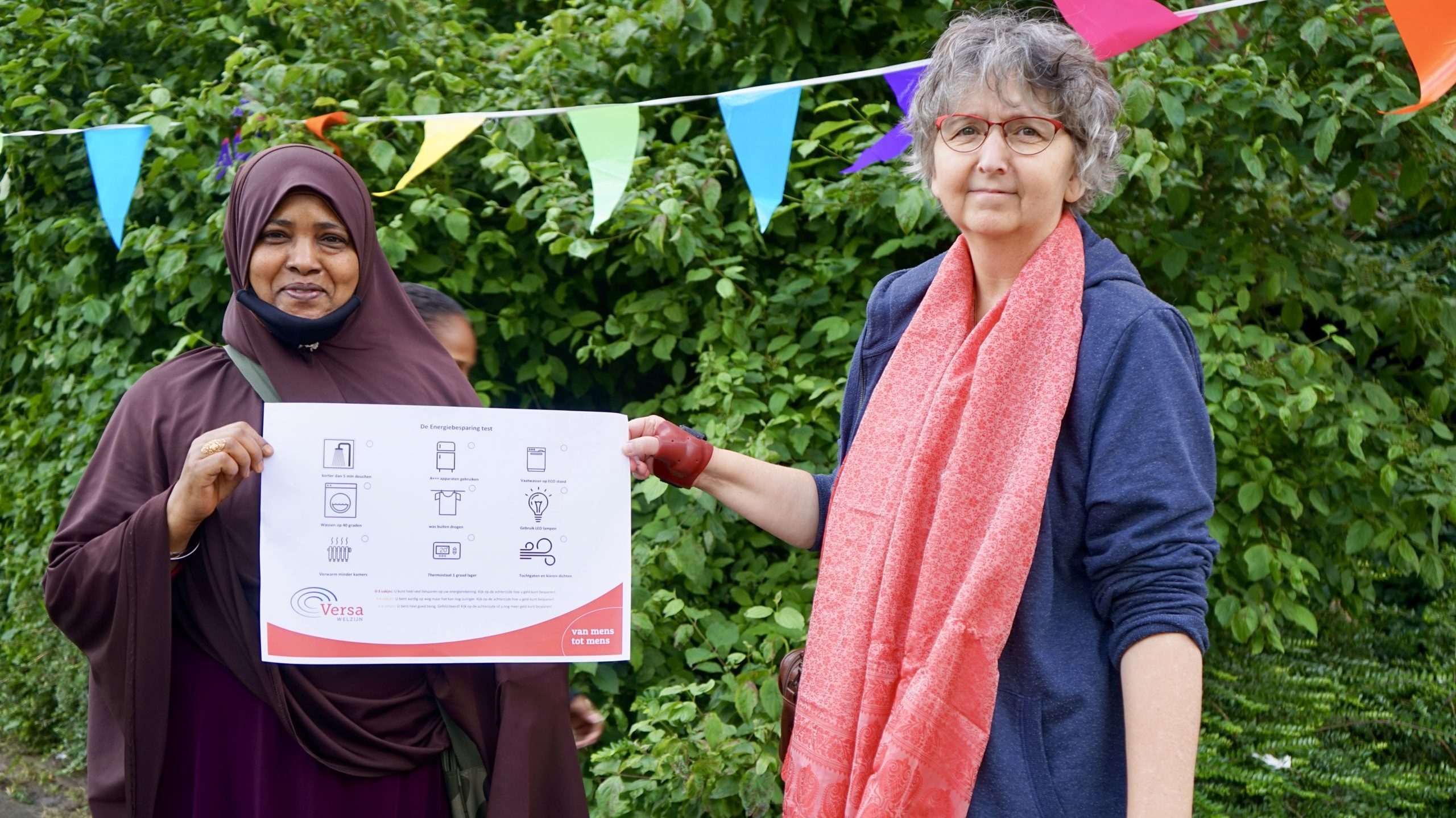 Twee vrouwen tonen informatieve poster over energiebesparing tijdens buurtbijeenkomst