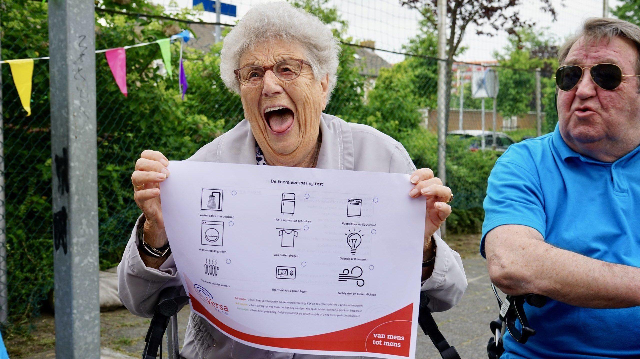 zittende vrouw op rollator toont affiche over energiebesparing tijdens buurtbijeenkomst