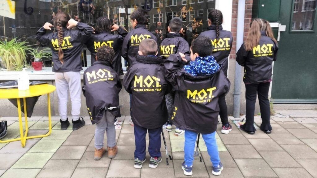 Een groepje kinderen poseren met zwarte jassen met op de rug de letters M.O.T.
