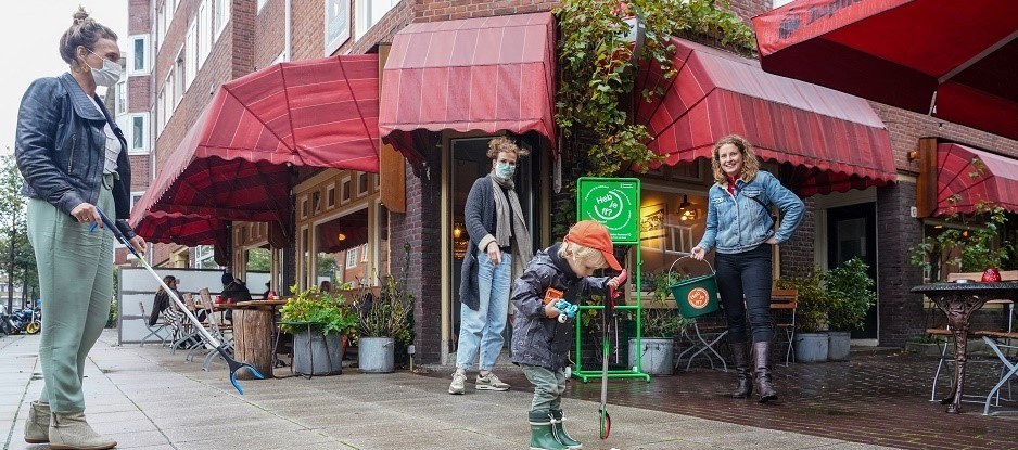 Drie vrouwen en een kind staan met een afvalgrijper voor een café